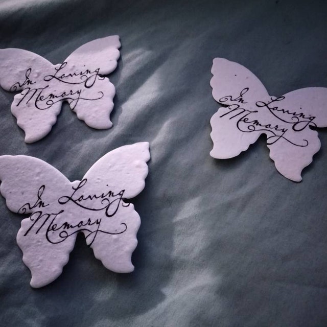 Seed paper butterflies with in loving memory message printed on a pale blue background